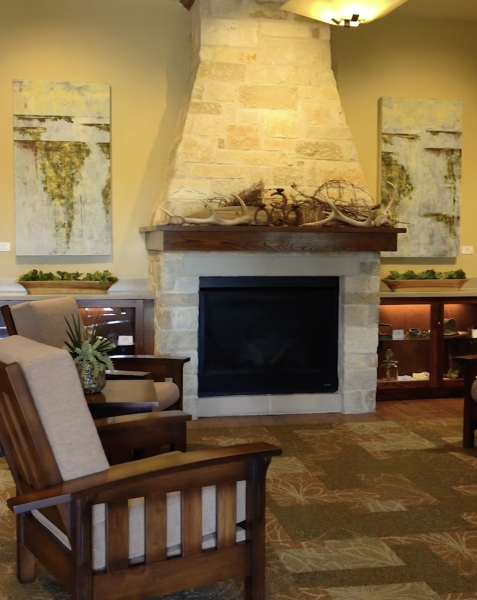 A cozy sitting area with armchairs facing a stone fireplace adorned with rustic decor and art pieces on the walls.